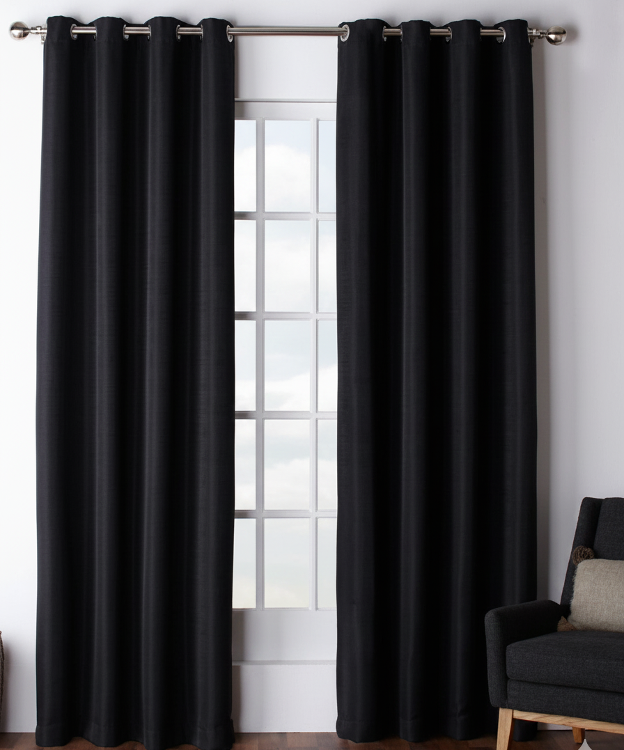 Black curtains hanging in front of a window with a chair on a wooden floor.